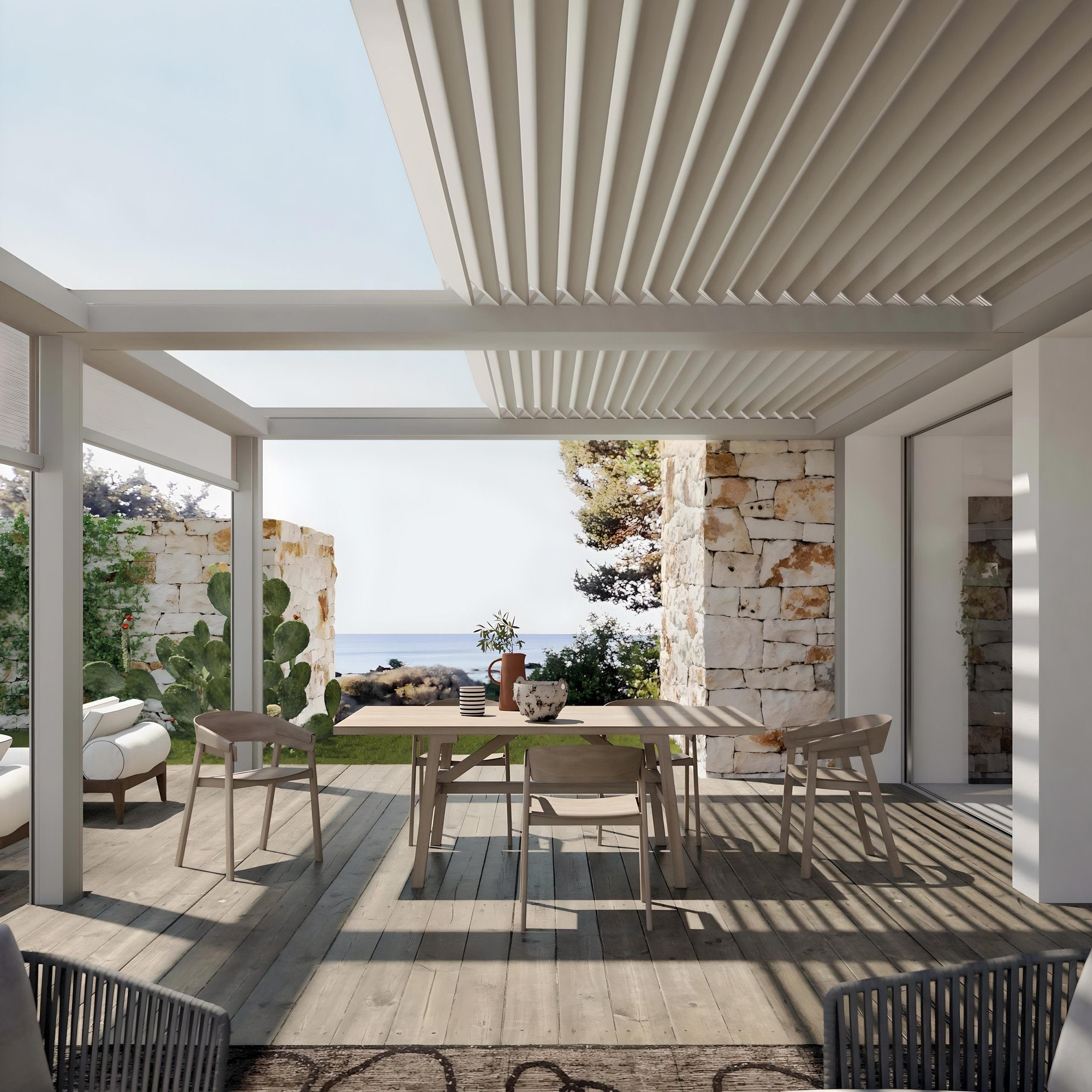 Pergola addossata con struttura in alluminio e copertura a lamelle orientabili, arredata con tavolo da pranzo e sedie in legno, affacciata su un giardino con vista mare.