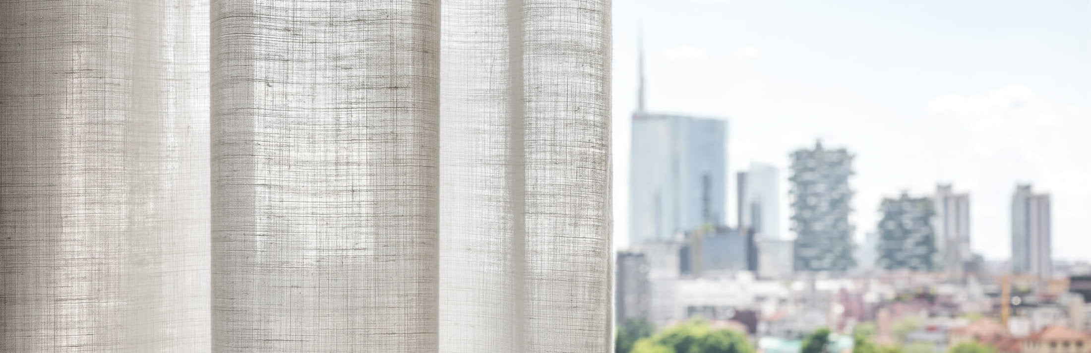 Dettaglio di tende per interni in tessuto chiaro con skyline di Milano sullo sfondo – Domotea Milano, soluzioni per ambienti luminosi