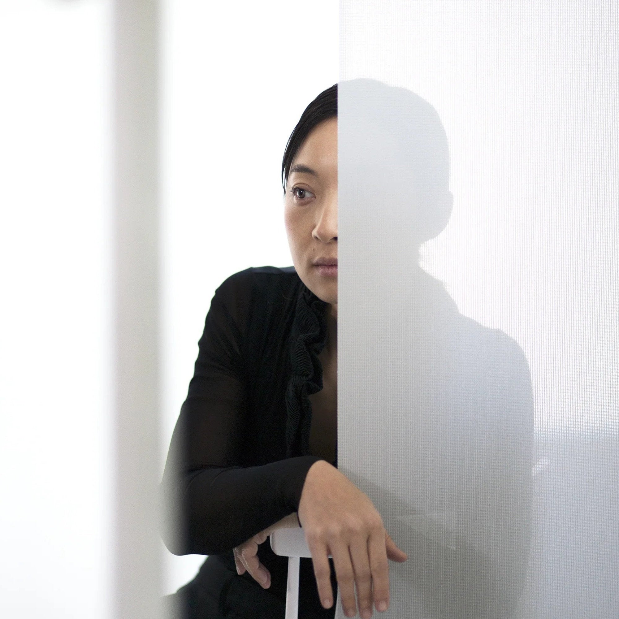 Donna seduta dietro una tenda a pannello bianca semitrasparente in un ambiente luminoso e minimale.
