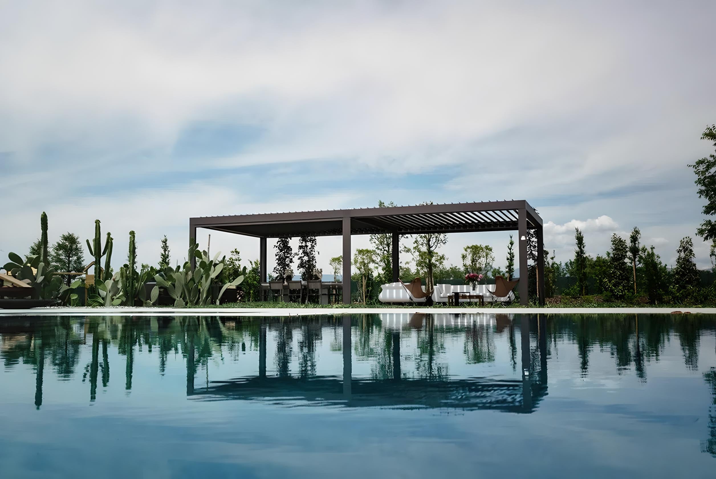 Pergola bioclimatica moderna posizionata a bordo piscina, con arredi da esterno e piante mediterranee – Domotea Milano, soluzioni outdoor per giardini e terrazze