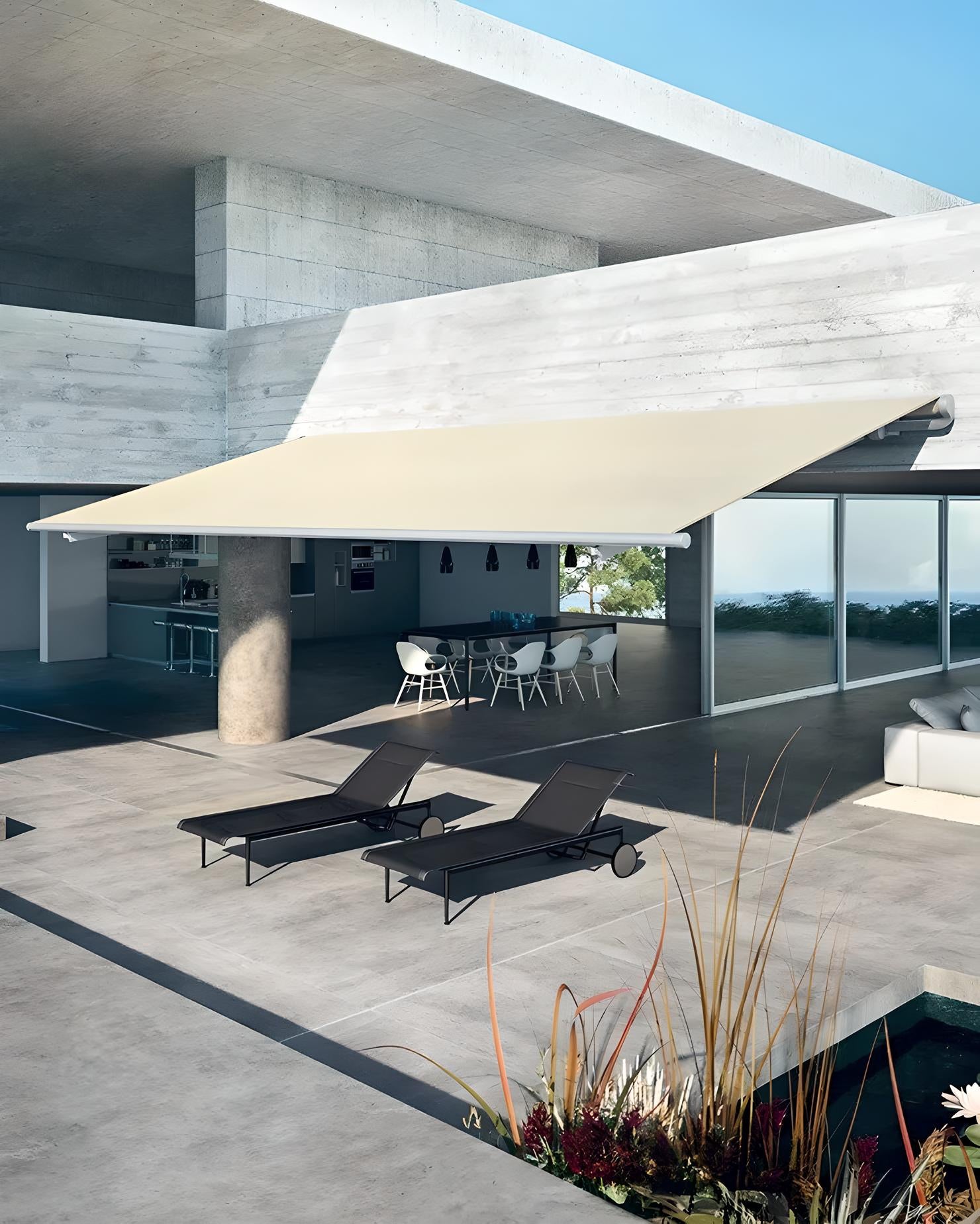 Tenda da sole a bracci color chiaro installata su terrazza di villa moderna con zona pranzo esterna e lettini, proposta Domotea Milano.