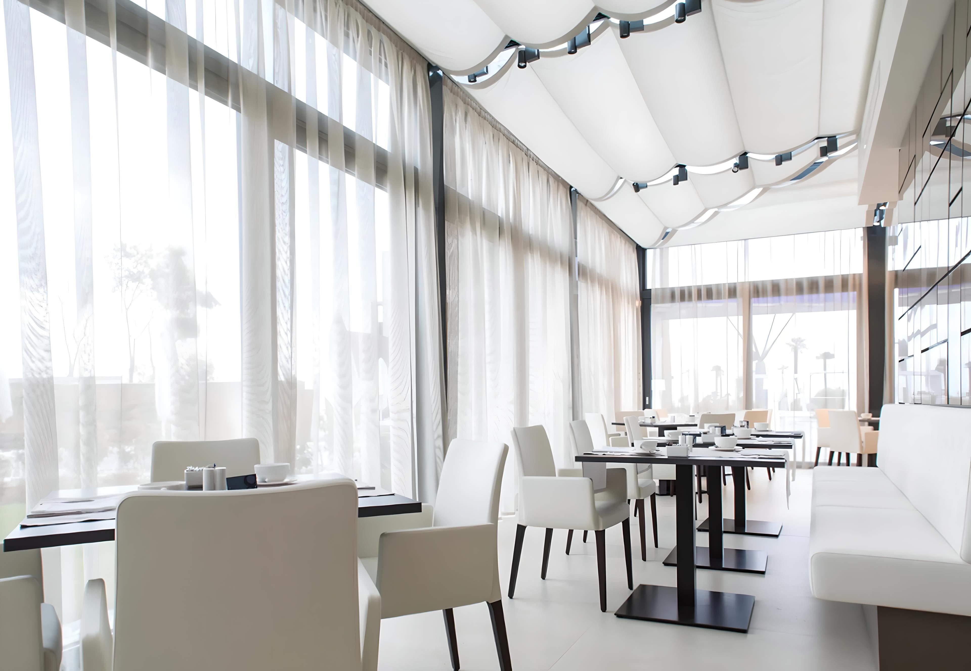 Sala da pranzo con ampie vetrate schermate da tende arricciate chiare – Domotea Milano, soluzioni per interni eleganti e filtraggio luce naturale