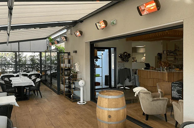 Riscaldatori Heliosa installati a parete sopra i tavoli di un dehors coperto.